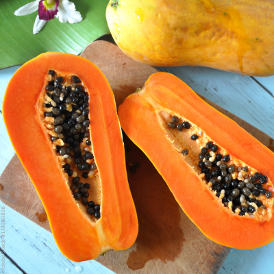 Eine frische Papaya liegt halbiert auf einem Holzbrett